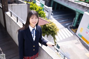 A woman in a school uniform leaning against a wall.