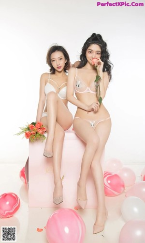 A couple of women sitting on top of a pink box.