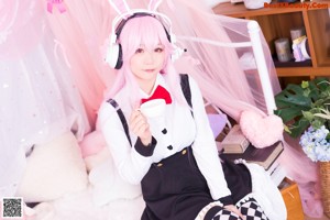A woman with pink hair wearing headphones on a bed.