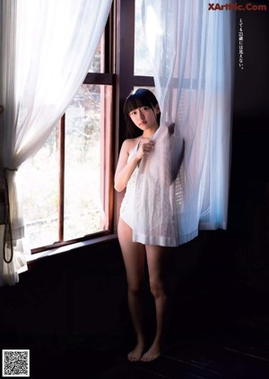 A woman with long black hair sitting on a bed.