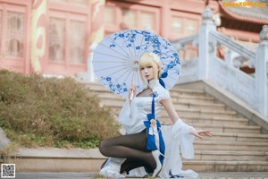 A woman in a white dress holding a blue and white umbrella.
