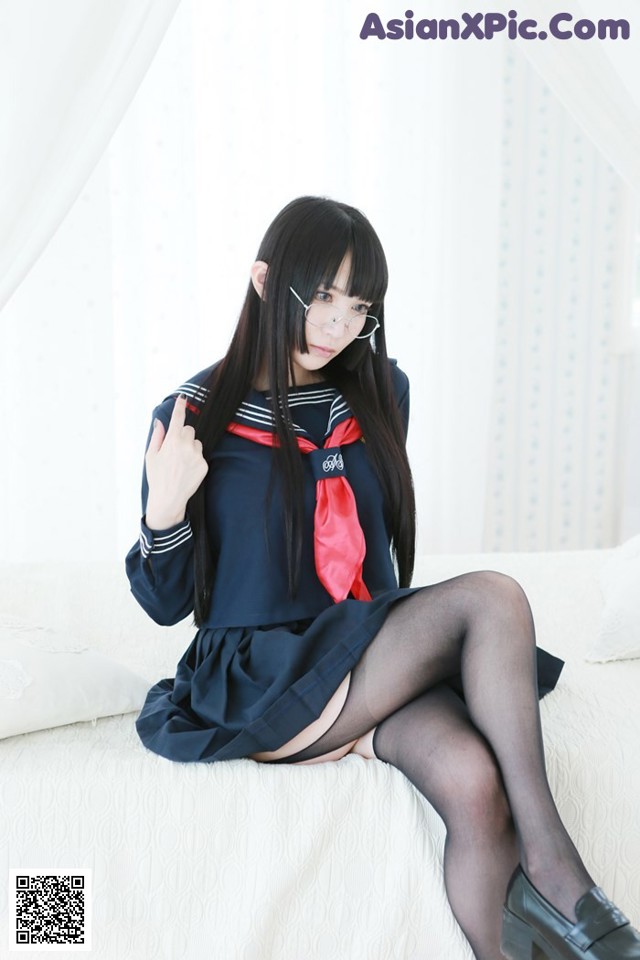 A woman in a school uniform sitting on a bed.