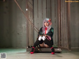 A woman in a black and red outfit is tied up in a cage.