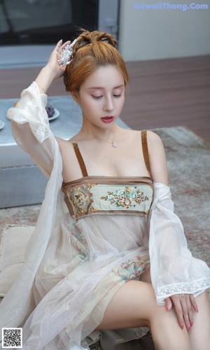 A woman in a white dress sitting on a pink chair.