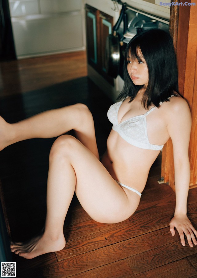 A woman in a white bra and panties sitting on the floor.