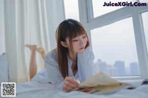 A woman sitting on a bed holding a magazine.