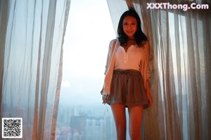 A woman standing in front of a window looking out at the city.