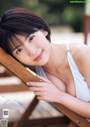 A woman in a white tank top sitting on a brown chair.
