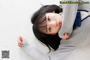 A woman in a red sweater leaning against a wall.