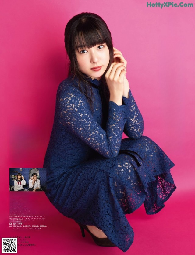 A woman in a blue dress sitting on a pink background.