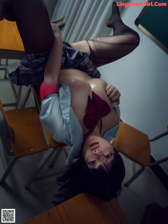 A woman laying on top of a desk in a classroom.